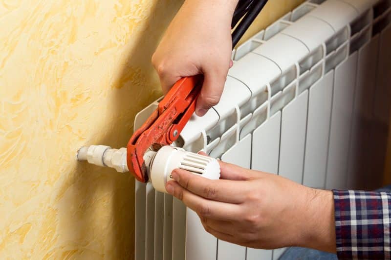 Closeup shot of man installing heating radiator and connecting valve