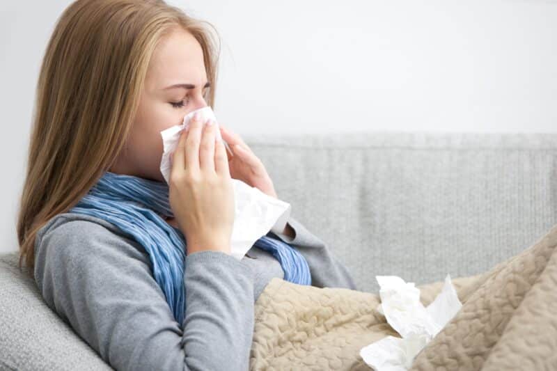 woman blowing her nose while sitting on the couch in her houston home due to seasonal allergies