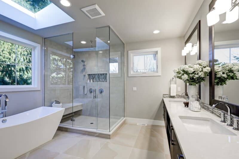 a modern master bathroom with a white soaking tub, glass shower and two sinks